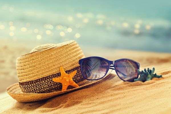 مفهوم تعطیلات تابستانی با کلاه حصیری و عینک آفتابی در ساحل شنی