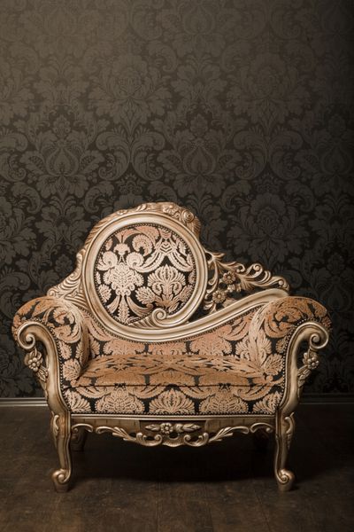 صندلی قهوه ای مایل به خاکستری قدیمی با لهجه های طلایی کنار دیوار ایستاده است کف چوبی