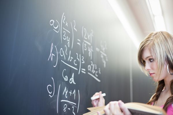 دانشجوی جوان زیبا که در طول کلاس ریاضی روی تخته سیاه می‌نویسد تصویر رنگی با رنگ کم عمق