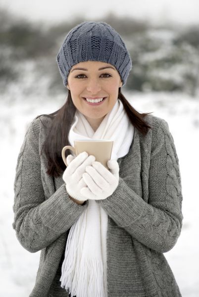 زن خندان در حالی که نوشیدنی در بیرون در برف نگه داشته است