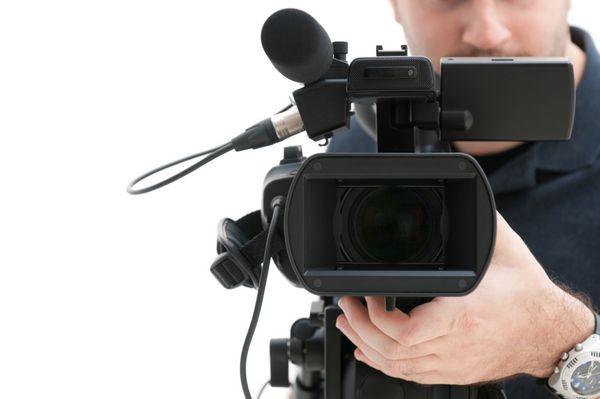 اپراتور دوربین فیلمبرداری که با تجهیزات حرفه ای خود جدا شده در پس زمینه سفید کار می کند
