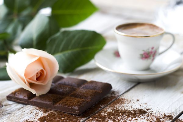 قهوه ترک با گل رز هلویی رنگ و تکه های شکلات روی میز چوبی
