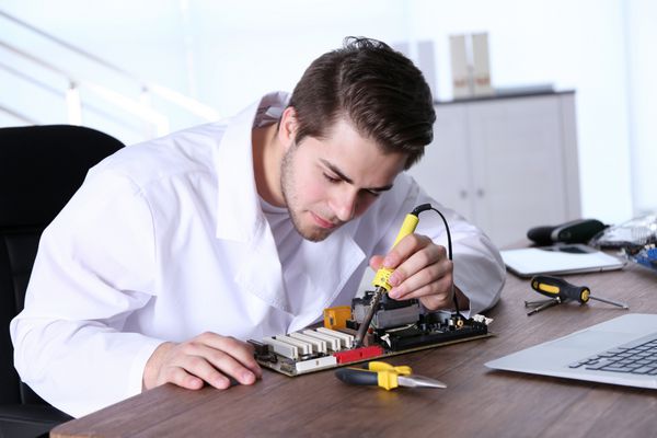 مردی با کت سفید در حال تعمیر مدارهای الکترونیکی در مرکز خدمات