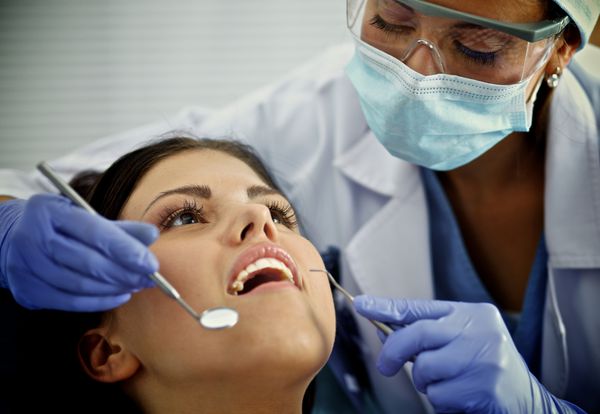 زن دندانپزشکی که روی دندان های بیمارش کار می کند