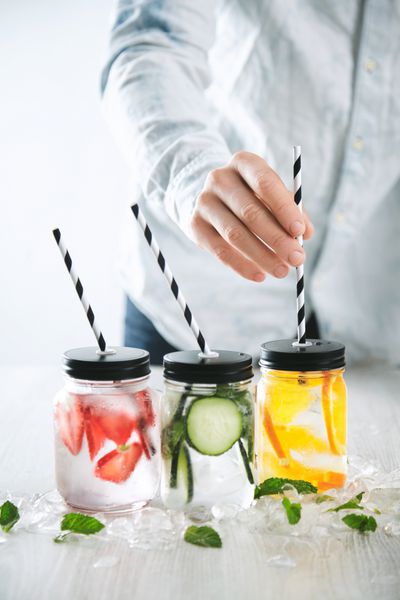 تند نی های راه راه نوشیدنی را با لیمونادهای خانگی سرد تازه ساخته شده از یخ توت فرنگی پرتقال خیار و نعناع در شیشه ها قرار می دهد یخ ذوب شده در اطراف نوشیدنی های خنک برای تابستان