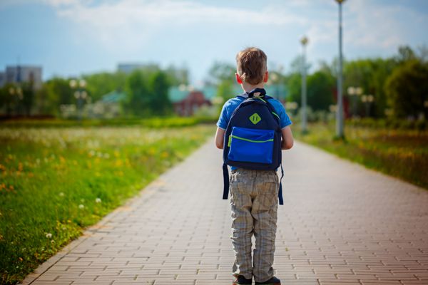 پسر کوچک با کوله پشتی به مدرسه می رود نمای پشتی