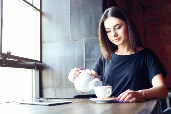 پرتره دختر جوان جذاب در حال ریختن چای در کافی شاپ در حالی که در اوقات فراغت به تنهایی در کافی شاپ نشسته است سبک زندگی قهوه