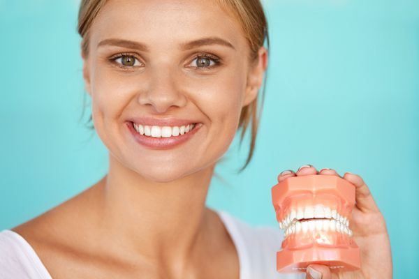 زنی با لبخند زیبا دندان های سالم که مدل دندانی در دست دارد تصویر با وضوح بالا