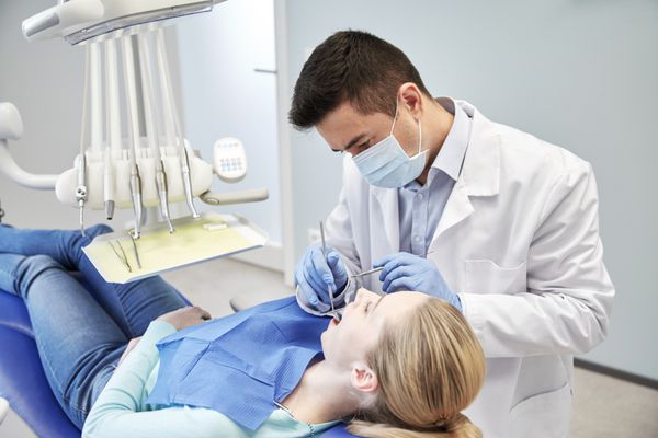 دندانپزشک مرد با ماسک در حال بررسی دندان های بیمار زن