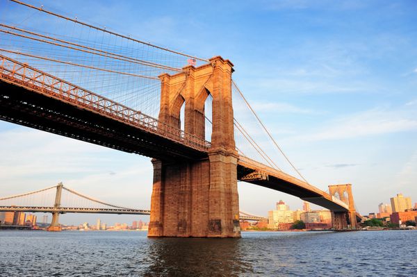 پل بروکلین بر روی رودخانه شرقی که از اسکله منهتن پایین شهر نیویورک در غروب آفتاب مشاهده می شود