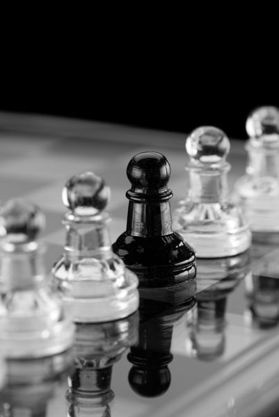 مهره های شطرنج شیشه ای روی صفحه شطرنج شیشه ای با انعکاس روی پس زمینه سیاه می تواند به عنوان مفهومی برای فردیت استفاده شود
