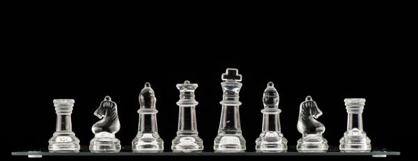 مهره های شطرنج شیشه ای شفاف روی صفحه شطرنج شیشه ای جدا شده روی پس زمینه سیاه