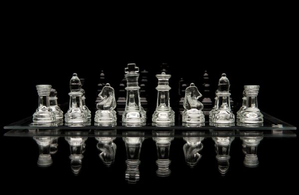 مهره های شطرنج شیشه ای روی صفحه شطرنج شیشه ای با انعکاس ایزوله شده روی پس زمینه سیاه