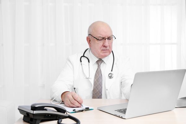 پرتره پزشک حرفه ای روی میز در مطب خود در پس زمینه پرده سفید