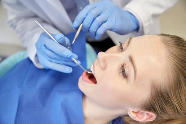 مفهوم مردم پزشکی دهان شناسی و مراقبت های بهداشتی - نمای نزدیک از دست های دندانپزشک با آینه و پروب دندان در حال بررسی دندان های بیمار زن در مطب کلینیک دندانپزشکی