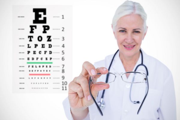 بینایی‌شناس زن خندان در حال ارائه عینک در برابر آزمایش چشم