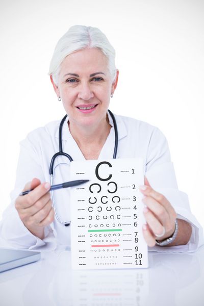 پرتره پزشک زن خندان که دفترچه یادداشت و خودکار را پشت میز در برابر آزمایش چشم در دست دارد