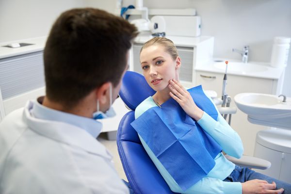 مردم پزشکی دهان و دندان و مفهوم مراقبت های بهداشتی - بیمار زن در حال صحبت با دندانپزشک مرد و شکایت از دندان درد در مطب کلینیک دندانپزشکی