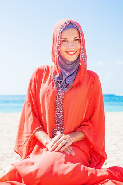 زن زیبای مسلمان قفقازی روسی با لباس قرمز در حال استراحت در ساحل