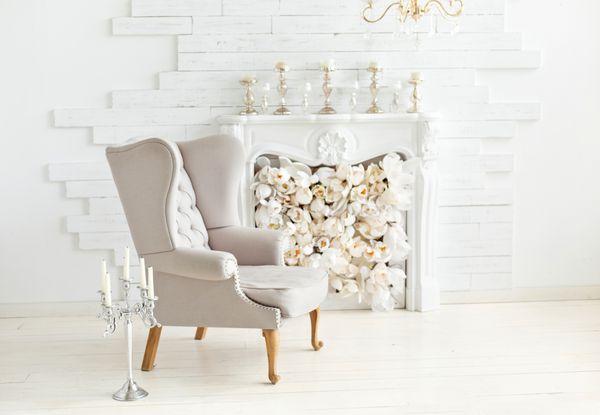 صندلی بغل نرم و زیبا در نزدیکی آتشدان فضای داخلی لوکس در رنگ های سفید صندلی راحتی با روکش پارچه ای
