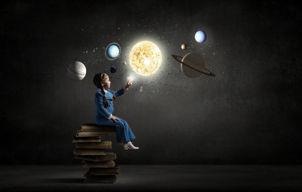 دختر کوچکی که روی پشته کتاب نشسته و سیاره را لمس می کند