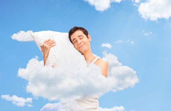 مرد شادی که خوابیده و بالشی نرم را در ابرهای آسمان در آغوش گرفته است