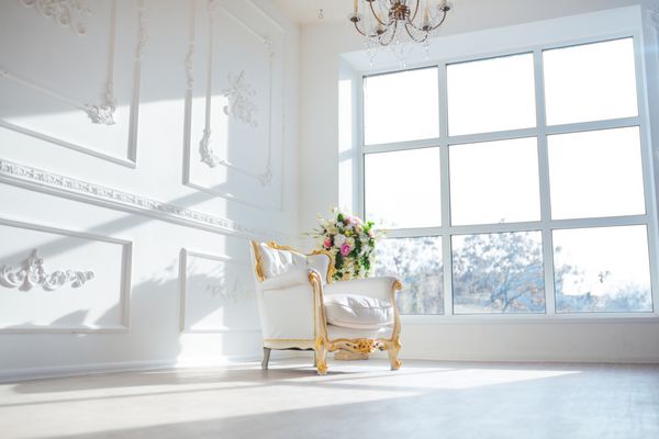 صندلی سبک چرم سفید در اتاق داخلی کلاسیک با پنجره بزرگ و گل های بهاری