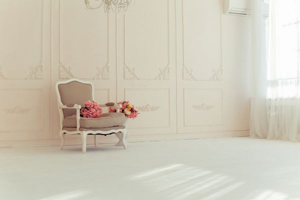 فضای داخلی لوکس در رنگ های بژ صندلی راحتی قدیمی در یک اتاق بزرگ با دیواری تزئین شده با زیور آلات گل های رنگارنگ در گلدانی که روی زمین چوبی ایستاده اند