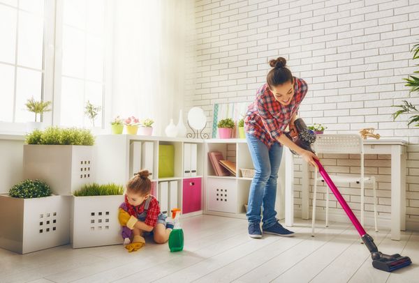 خانواده شاد اتاق را تمیز می کنند مادر و دختر نظافت خانه را انجام می دهند زن جوان و دختر بچه ای گرد و غبار را پاک کردند و زمین را جاروبرقی کشیدند