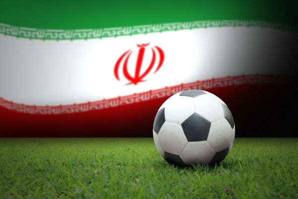 توپ سیاه و سفید فوتبال قدیمی روی چمن سبز دارای پس زمینه پرچم ملی ایران است