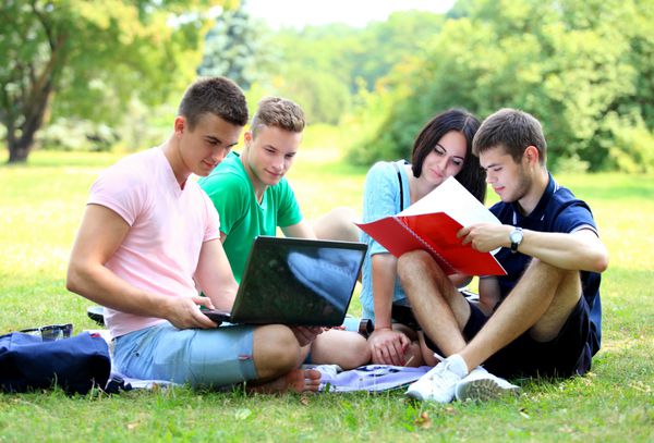 چهار دانش آموز خندان در حال مطالعه در پارک سبز