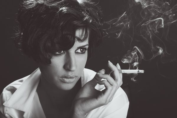 زن زیبا در حال کشیدن سیگار در پس زمینه سیاه