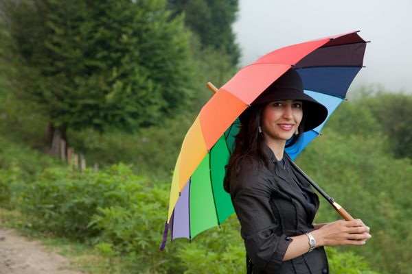 خانم زیبا با کلاه سیاه و چتر رنگارنگ در جنگل ابری