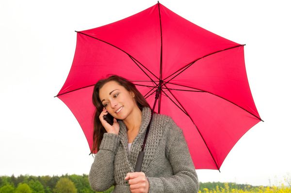 زن جوان با تلفن همراه زیر چتر