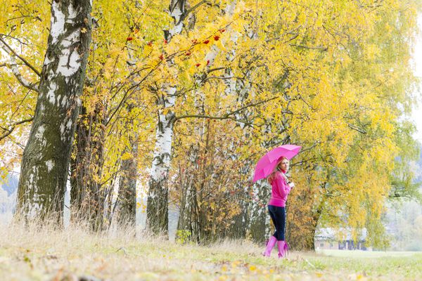 زنی که چکمه های لاستیکی با چتر در طبیعت پاییزی پوشیده است
