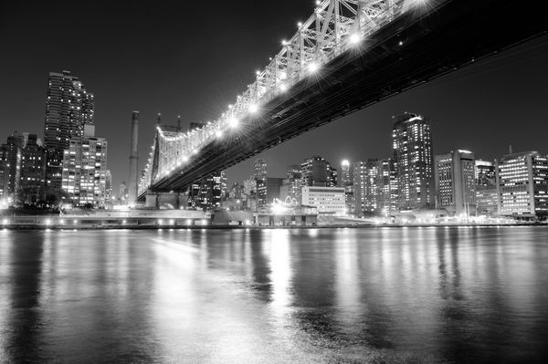 پل کوئینزبورو بر روی رودخانه شرقی شهر نیویورک در شب سیاه و سفید با انعکاس رودخانه و خط افق منهتن میدتاون روشن شده است