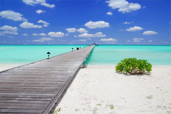 اسکله چوبی بر فراز ساحل زیبای مالدیو با آسمان آبی و ابرها