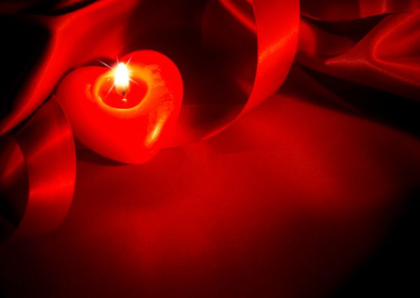 طرح شمع قلب و حاشیه ابریشم قرمز شمع های قرمز سوزان به شکل قلب و روبان ساتن قرمز روی زمینه ابریشم قرمز روز