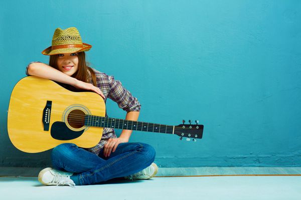 نوازندگی گیتار دختر نوجوان نشسته روی زمین پس زمینه آبی سبک کشور