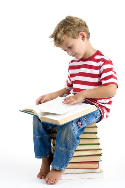 پسر پنج ساله ای که روی انبوهی از کتاب ها نشسته و مشغول مطالعه است