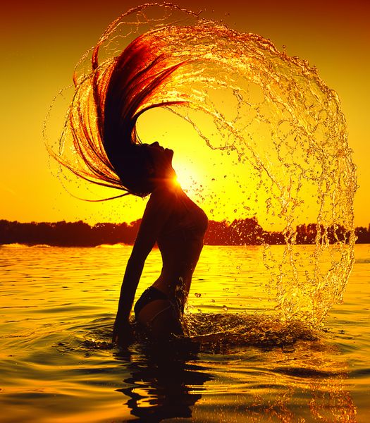 دختر مدل زیبایی که با موهایش آب می پاشد دختر نوجوان در حال شنا و آب پاشیدن در ساحل تابستانی بر فراز غروب آفتاب زن زیبا در آب