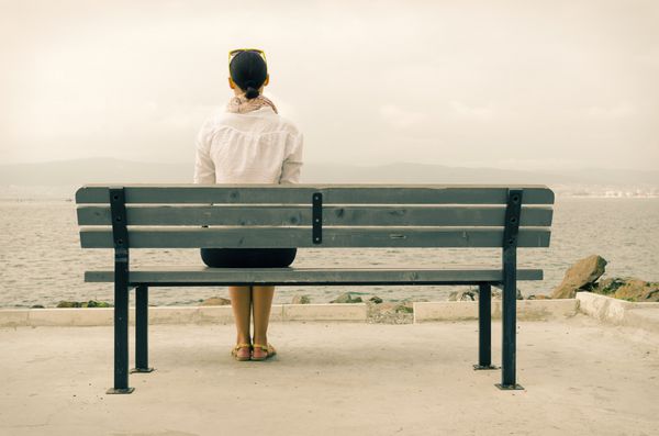 زن تنها نشسته روی نیمکت کنار دریا