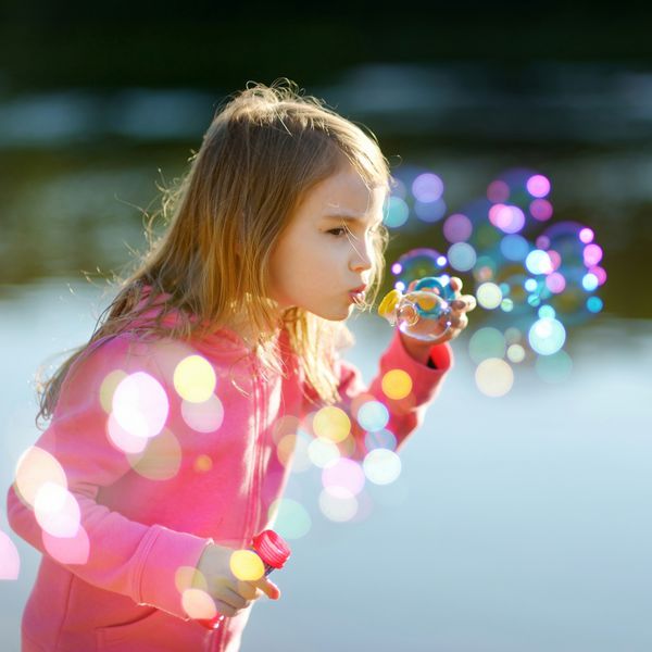 دختر بچه دوست داشتنی خنده دار که حباب های صابون را در غروب آفتاب در فضای باز می دمد