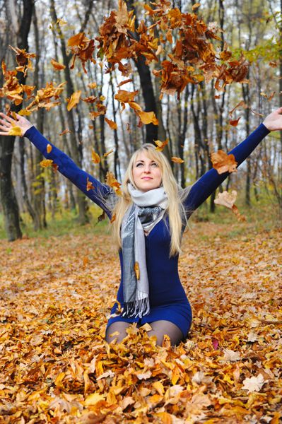 زن شاد زیبا با برگ های پاییزی در جنگل