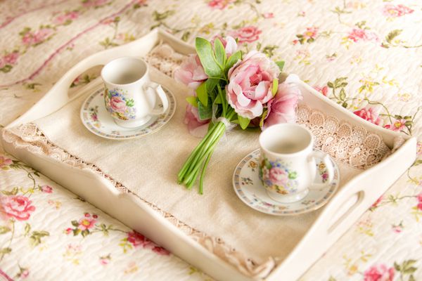نزدیک سینی قدیمی با گل و فنجان چای دراز کشیده روی تخت