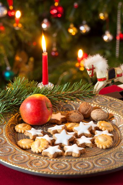 ترکیب با تزئینات کریسمس روی یک میز با رومیزی قرمز بشقاب با کلوچه اسباب بازی اسب و یک شمع قرمز روی شاخه صنوبر
