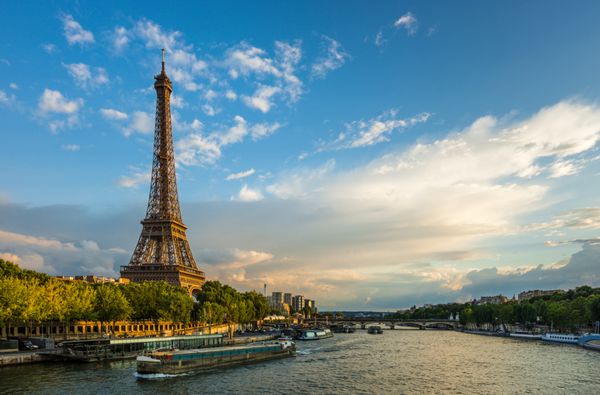 غروب زیبا بر فراز برج ایفل و رودخانه سن با ابرهای پف کرده پاریس فرانسه