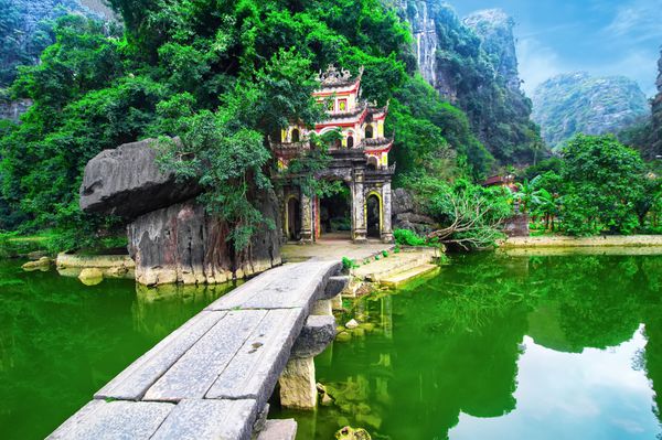 منظره پارک در فضای باز با دریاچه و پل سنگی ورودی دروازه مجتمع بتکده باستانی بیچ دونگ نین بین مقصد سفر ویتنام