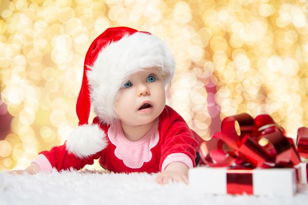 نوزاد کوچک زیبا کریسمس را جشن می گیرد تعطیلات سال نو کودک در لباس کریسمس با هدیه