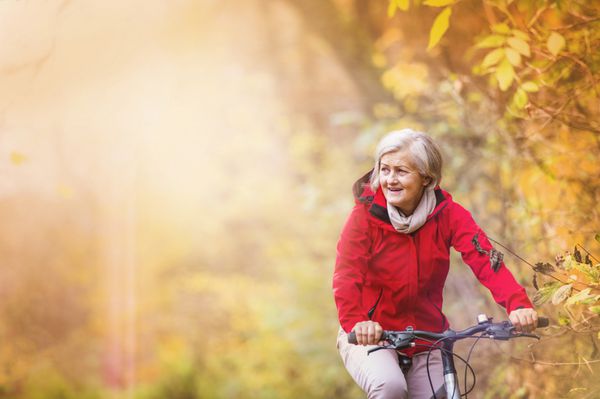 زن سالمند فعال دوچرخه سواری در طبیعت پاییزی